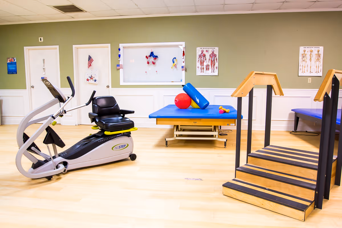 Physical therapy room with a recumbent NuStep exercise machine, a treatment table with therapy balls, and practice stairs.