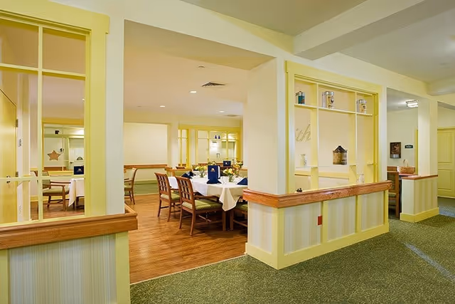 Well-lit dining area with multiple set tables and wooden chairs seen through a decorative partition.