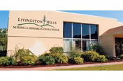 Exterior front of the Livingston Hills Nursing & Rehabilitation Center building with landscaped shrubs and large windows.