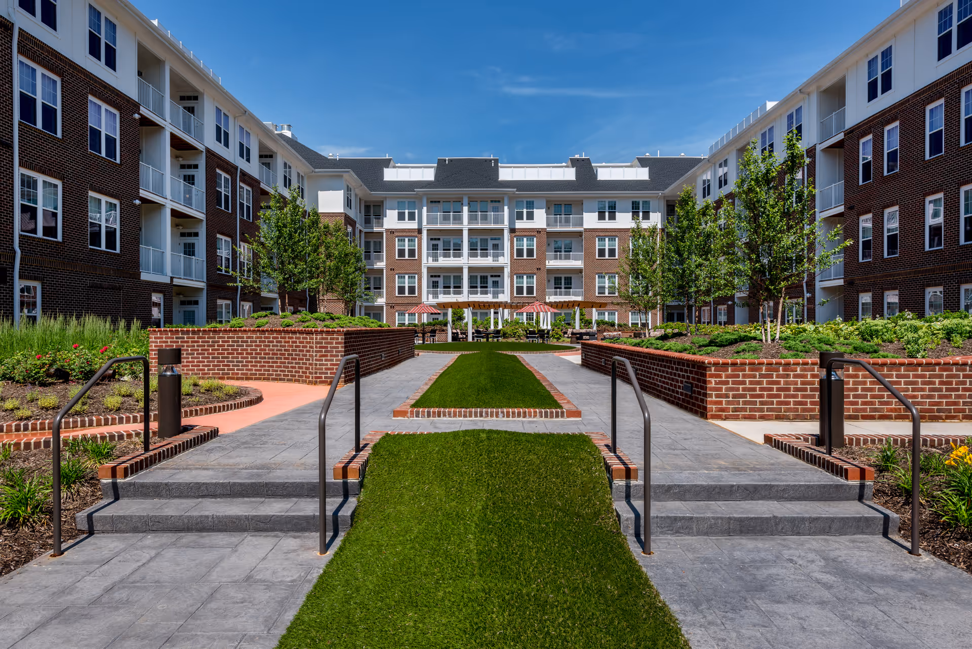 Central courtyard with grass walkways, brick planters, trees and a surrounding four-story brick residential building with balconies.