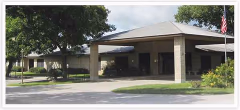 Front view of Floresville Nursing Center with canopied entrance and American flag.