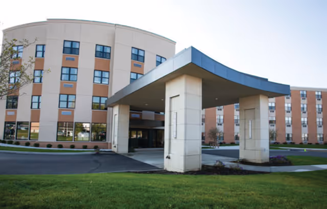 Front entrance of a multi-story senior living facility with a covered porte-cochere and landscaped lawn.