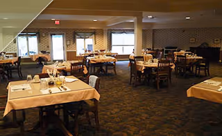 Spacious dining room with multiple tables set with place settings and wooden chairs, carpeted floor and windows.