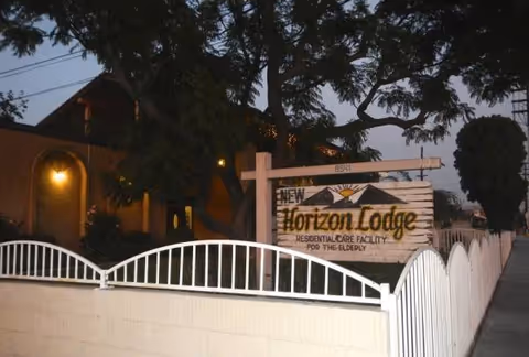 Entrance sign for New Horizon Lodge at a gated building front with trees