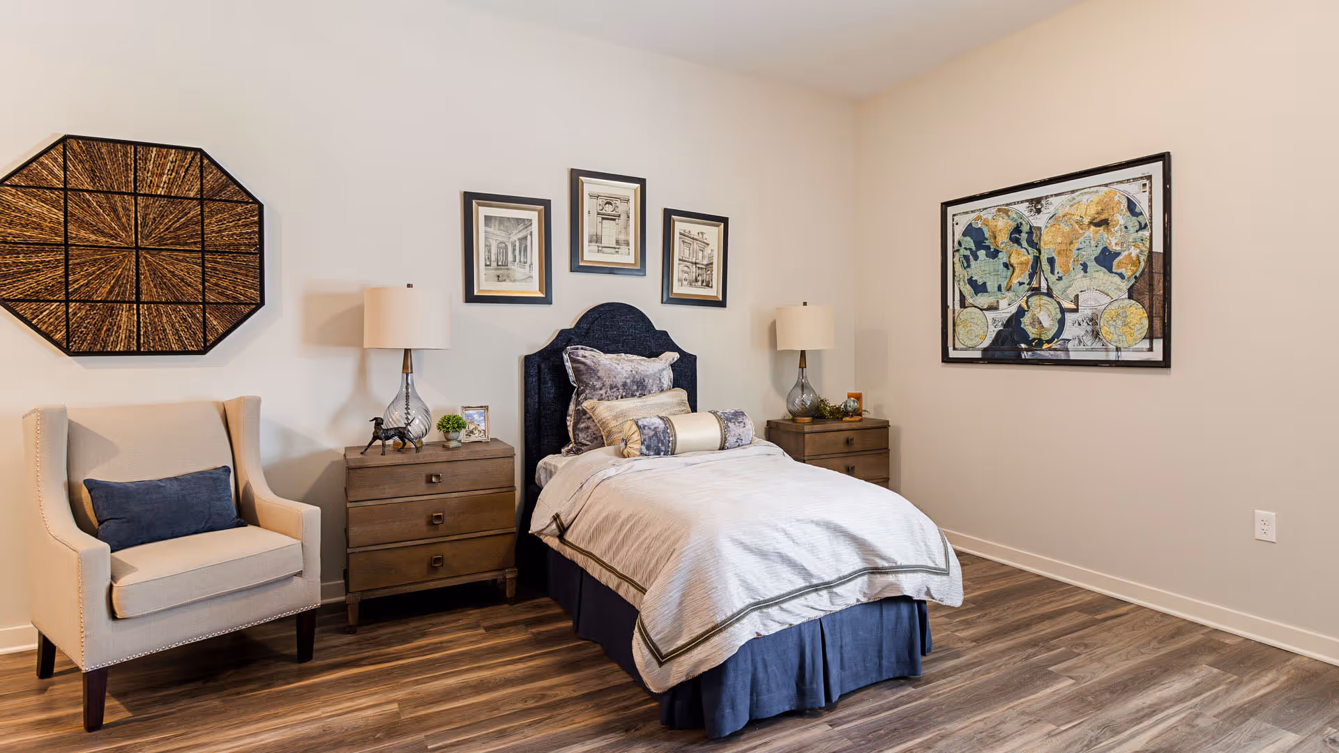 Single-bed bedroom with an upholstered headboard, two nightstands and lamps, an armchair, and framed wall art.