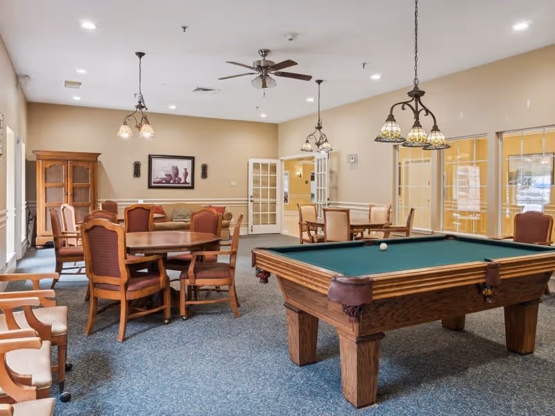 Well-lit senior community common room with a pool table, card tables, and seating.