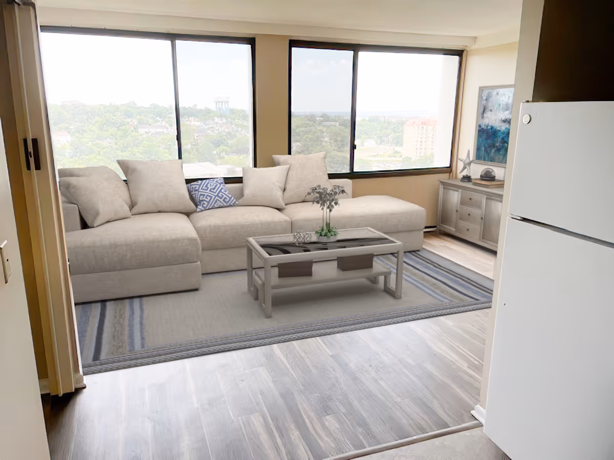 Spacious living room with a light-gray sectional sofa, coffee table on a rug, large windows with a view, and a refrigerator visible at the entry.