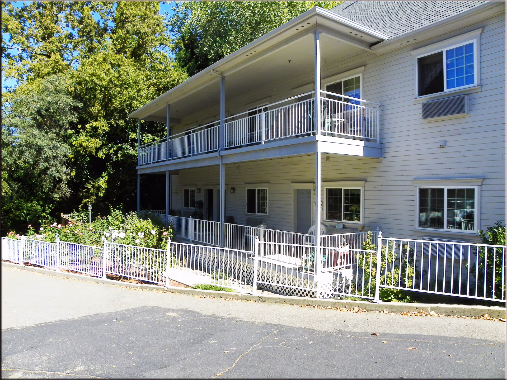 Two-story building with covered balconies, white railings and a fenced landscaped front area.