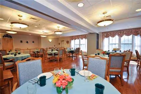 Bright dining room with round tables, chairs, and floral centerpieces.