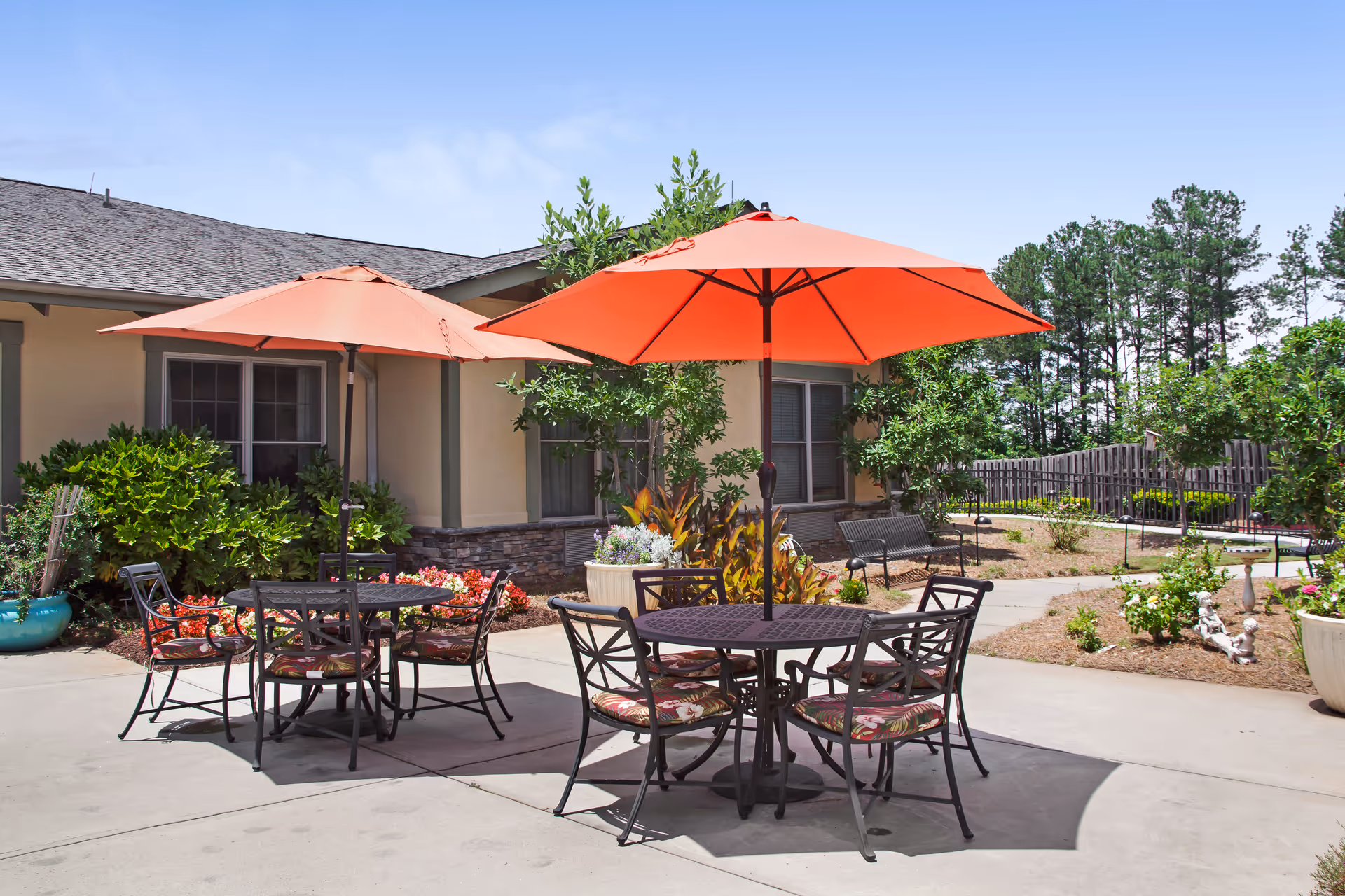 Outdoor courtyard patio with round tables, orange umbrellas, and chairs in front of a single-story building.