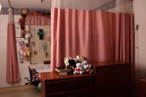A senior living facility bedroom with pink curtains, dresser, and stuffed animals.