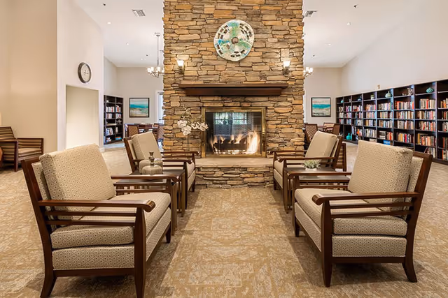 Cozy communal lounge with armchairs arranged around a central stone fireplace and bookshelves along the walls.