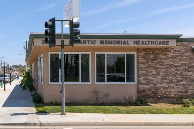 Exterior view of Atlantic Memorial Healthcare Center building with a traffic light pole in front and a sidewalk along the side. The building has beige walls with stone accents and several windows.