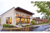 Modern senior living facility with large glass windows, beige brick exterior, and landscaped entrance.