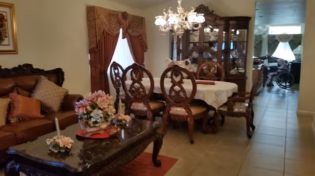 Elegant dining and living area with ornate wood furniture, chandelier, and floral accents.
