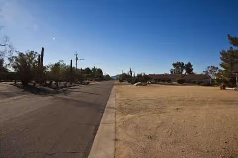 Desert street with sidewalk, leading to a distant Elder's Ranch building and campus.