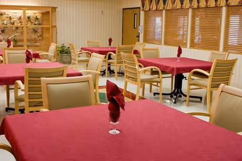 Empty senior dining room with red tablecloths and beige chairs.