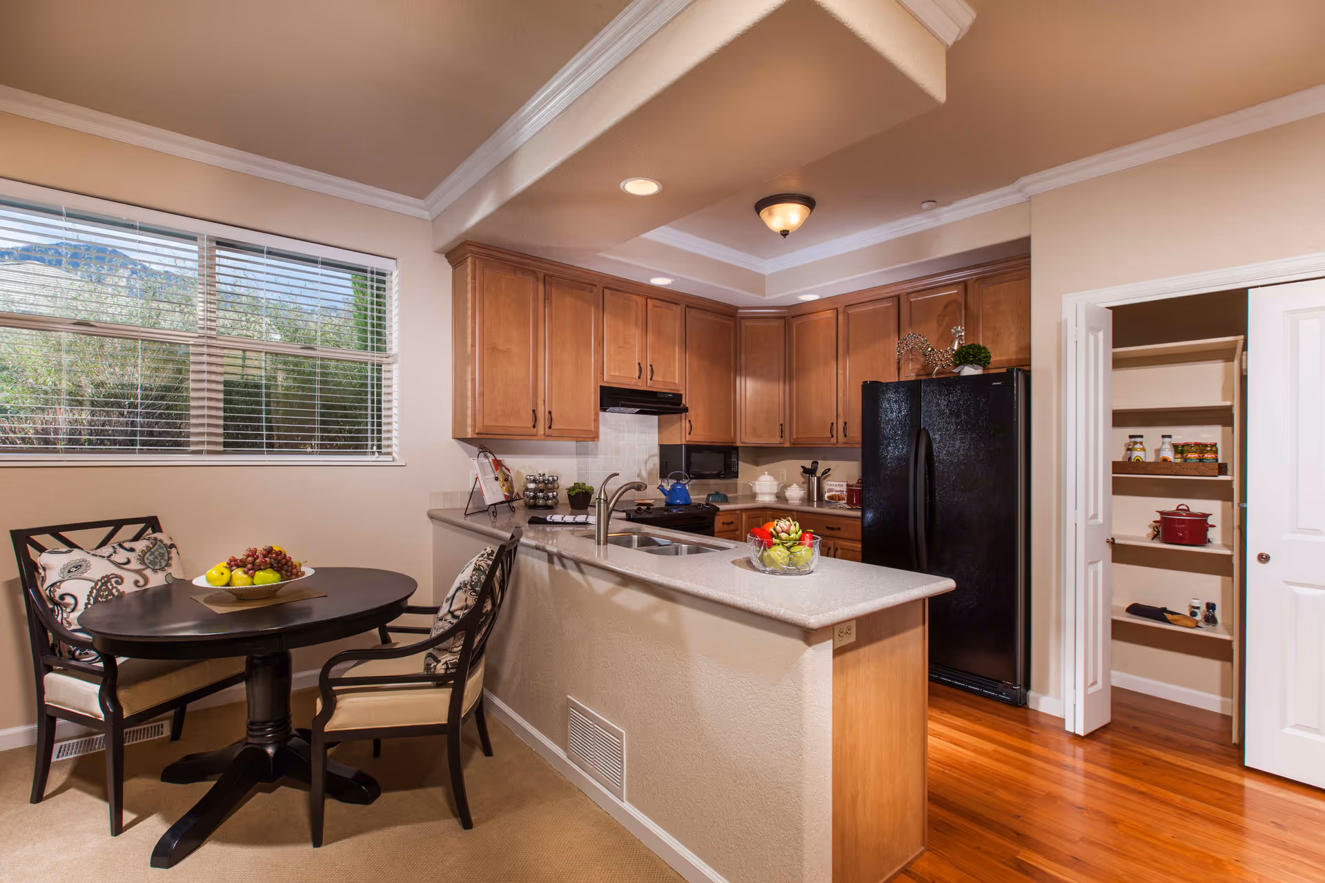 Open kitchen and breakfast nook with wooden cabinets, a black refrigerator, an island with sink, and a round dining table by a window.