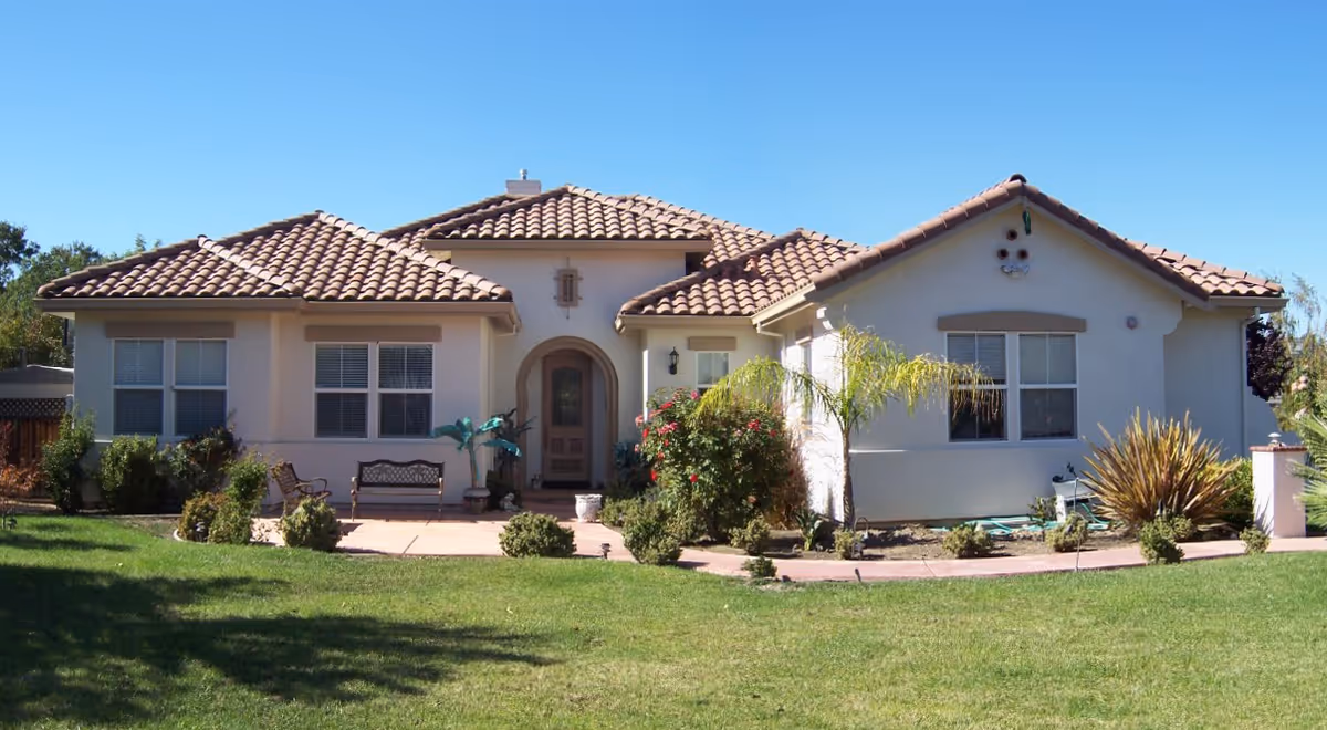 Front exterior of a single-story stucco house with a tiled roof, lawn, and landscaped yard.