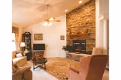 Cozy living room with a stone fireplace, armchairs and sofa around a coffee table under a ceiling fan.