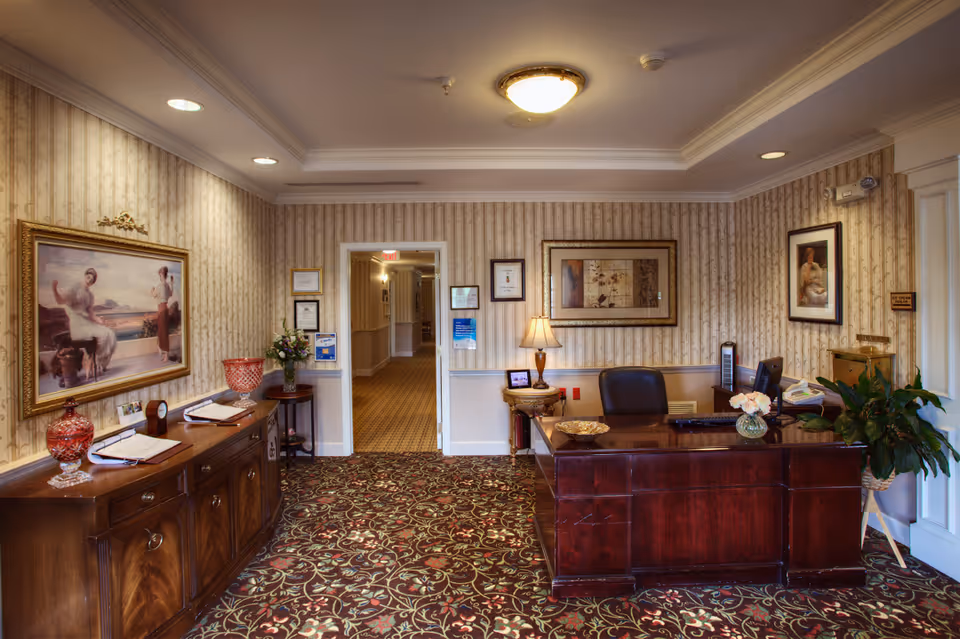 Reception desk and entrance hallway of a senior living facility with traditional furnishings and framed artwork.