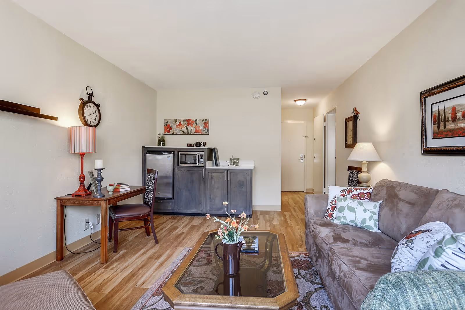 Living room of a senior living apartment with a sofa, coffee table, side table and a small kitchenette along the back wall.