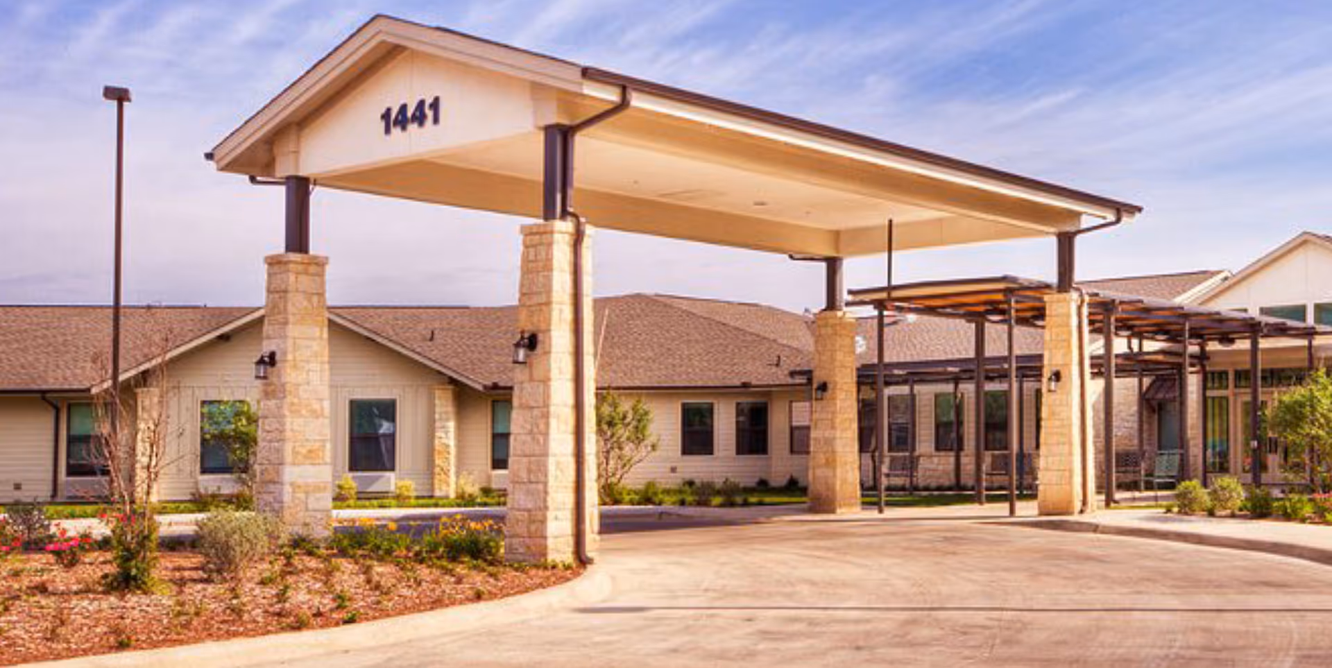 A covered porte-cochere with stone columns at the front entrance of a single-story building showing the number 1441.