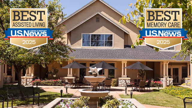 Exterior view of Claremont Place featuring a courtyard with a central water fountain, outdoor seating with tables and umbrellas, surrounded by a building with large windows and a peaked roof, and landscaped greenery and flowers.