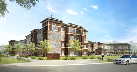 Exterior view of a multi-story senior living facility named SilverCreek on Main, featuring a modern design with stone and wood accents, surrounded by landscaped greenery and a clear blue sky. A car is parked on the street in front, and a person is walking on the sidewalk nearby.