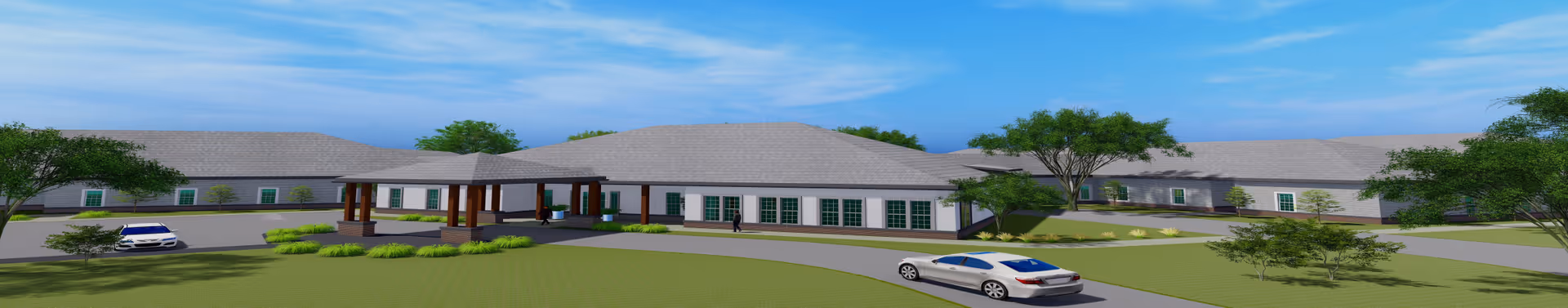 Wide exterior view of a single-story assisted living community building with a covered entrance, surrounded by green lawns, trees, and a few parked cars under a blue sky.