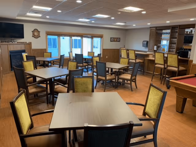 Interior view of a dining room with tables and chairs, featuring a bar area and large windows.