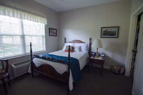 Traditional bedroom with a four-poster bed, nightstand, and two large windows.