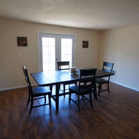 A dining room with a dark wooden table and six chairs in a simple interior.