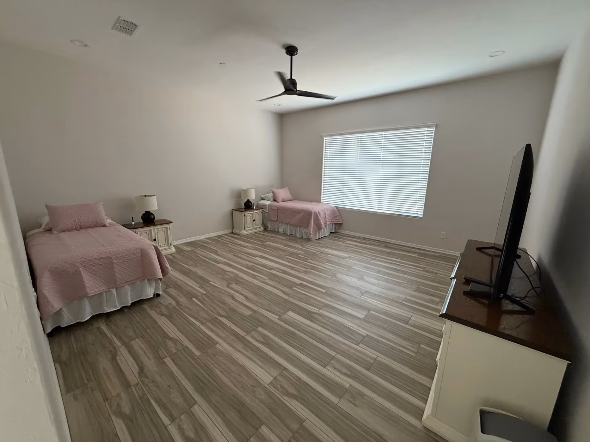 A spacious bedroom with two twin beds, pink quilts, and a dresser with TV.