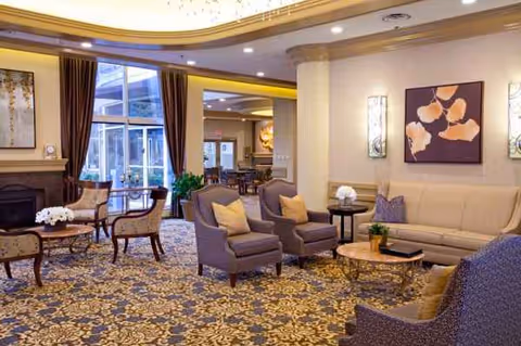 Elegant senior living lounge with cream sofas, armchairs, coffee tables, and floral carpet.