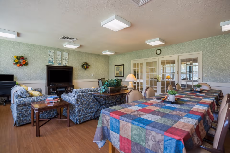 A common area with a colorful tablecloth, comfortable seating, and decorative wall accents, featuring a television and plants.