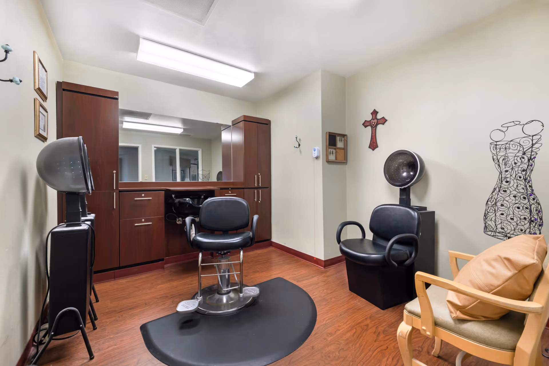 Interior salon room with a styling chair, hooded hair dryers, large mirror, wooden cabinets and additional seating.