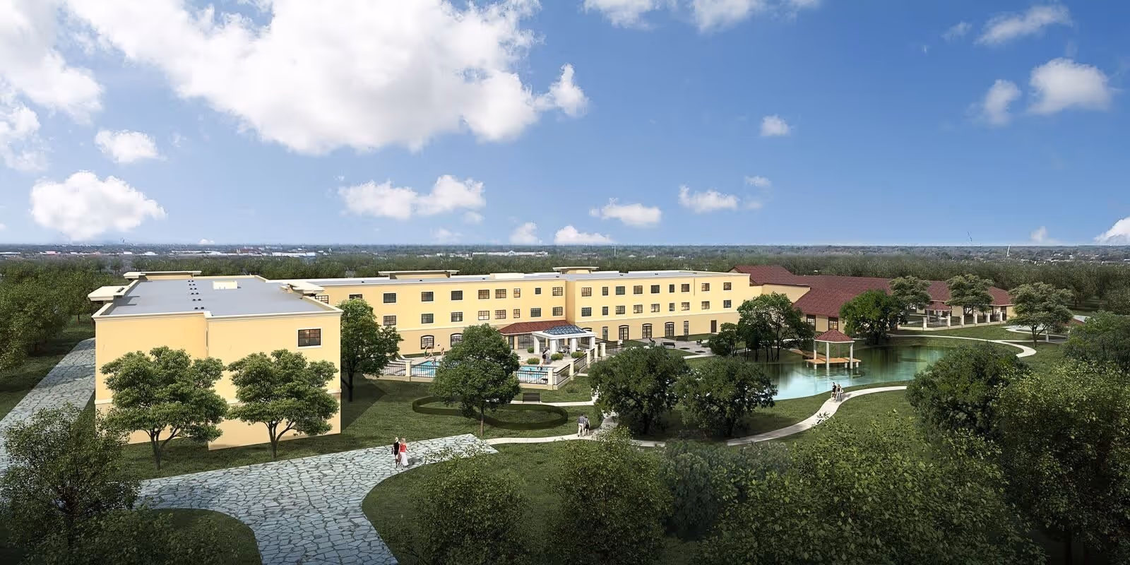 Aerial view of Laurel Glen at Sugar Land senior living facility showing a large, multi-story yellow building with a red roof section, surrounded by green lawns, trees, walking paths, and a pond with a small gazebo. The sky is blue with scattered clouds.