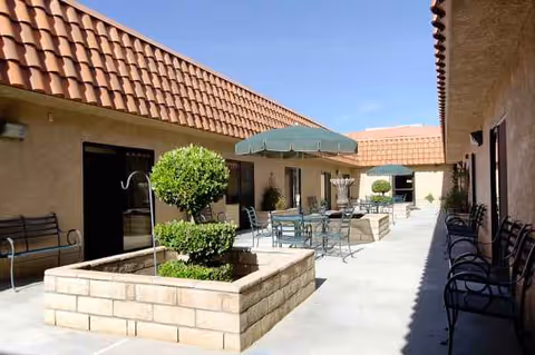 Outdoor patio area of Knolls West Residential Care with tables, umbrellas, and planters.