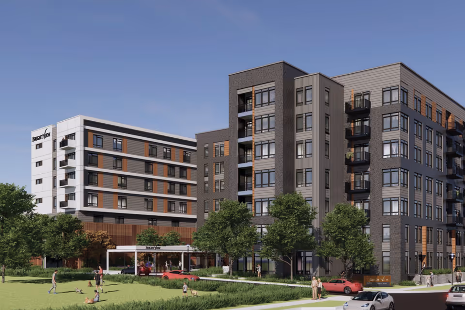 Exterior view of a modern multi-story senior living building with a lawn, trees, parked cars and people in front.