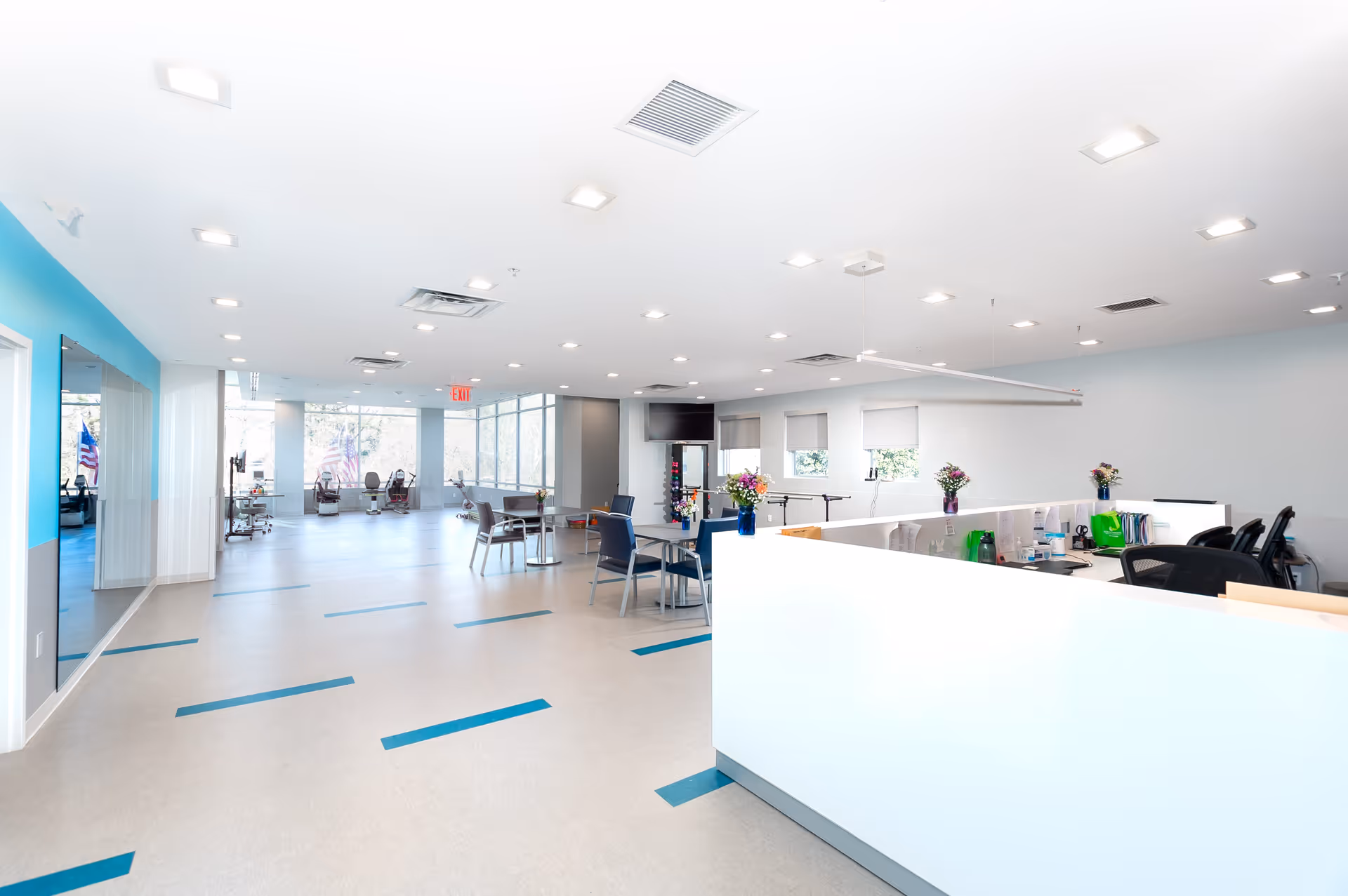 Bright, modern rehabilitation facility interior with a reception desk, tables and chairs and exercise equipment in an open, well-lit space.