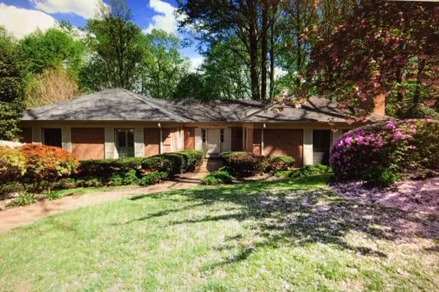Single-story brick building surrounded by green grass, bushes, and trees under a partly cloudy sky.