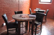Small dining area with round wooden tables and black leather chairs against exposed brick walls and a window.