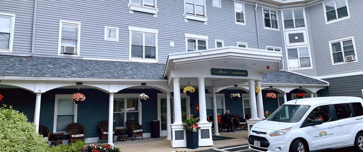 Exterior view of Cadbury Commons senior living facility with a covered entrance and seating.