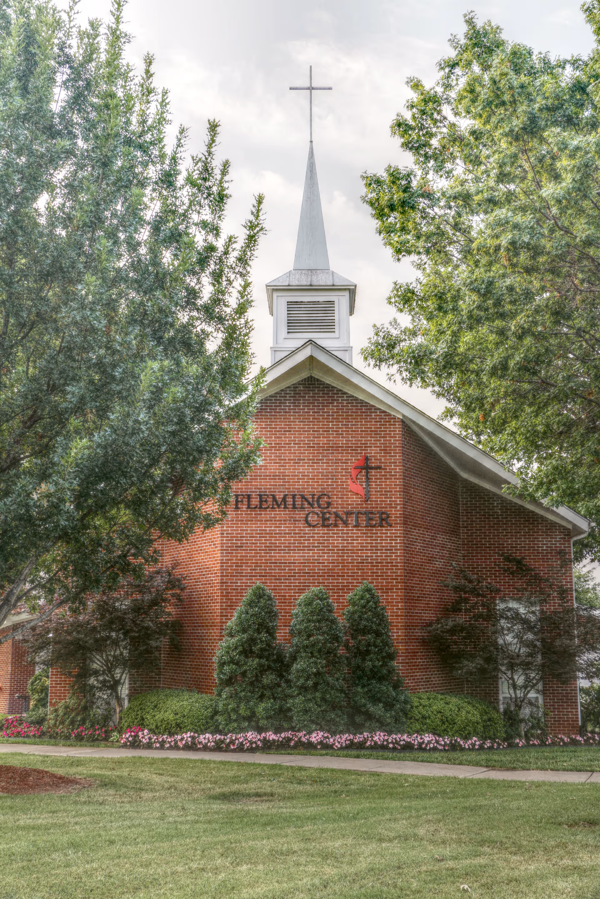 Brick community building with a white steeple and cross, surrounded by trees and landscaping and labeled 'FLEMING CENTER'.