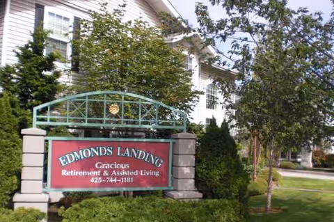Front exterior view of Edmonds Landing sign with a building and trees.