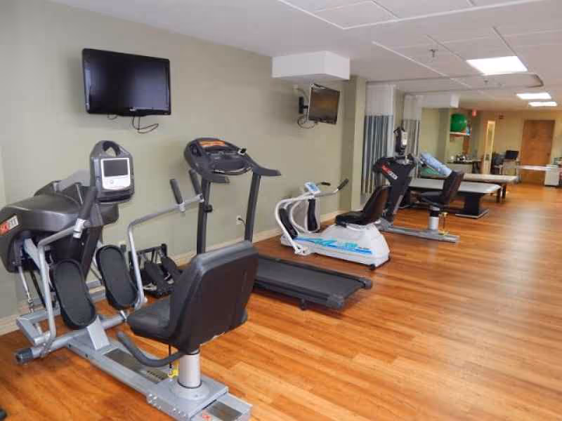 Fitness room with treadmills, recumbent bikes and wall-mounted TVs on wood floors.