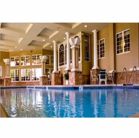 Indoor swimming pool with columns, large windows, and seating along the tiled deck.
