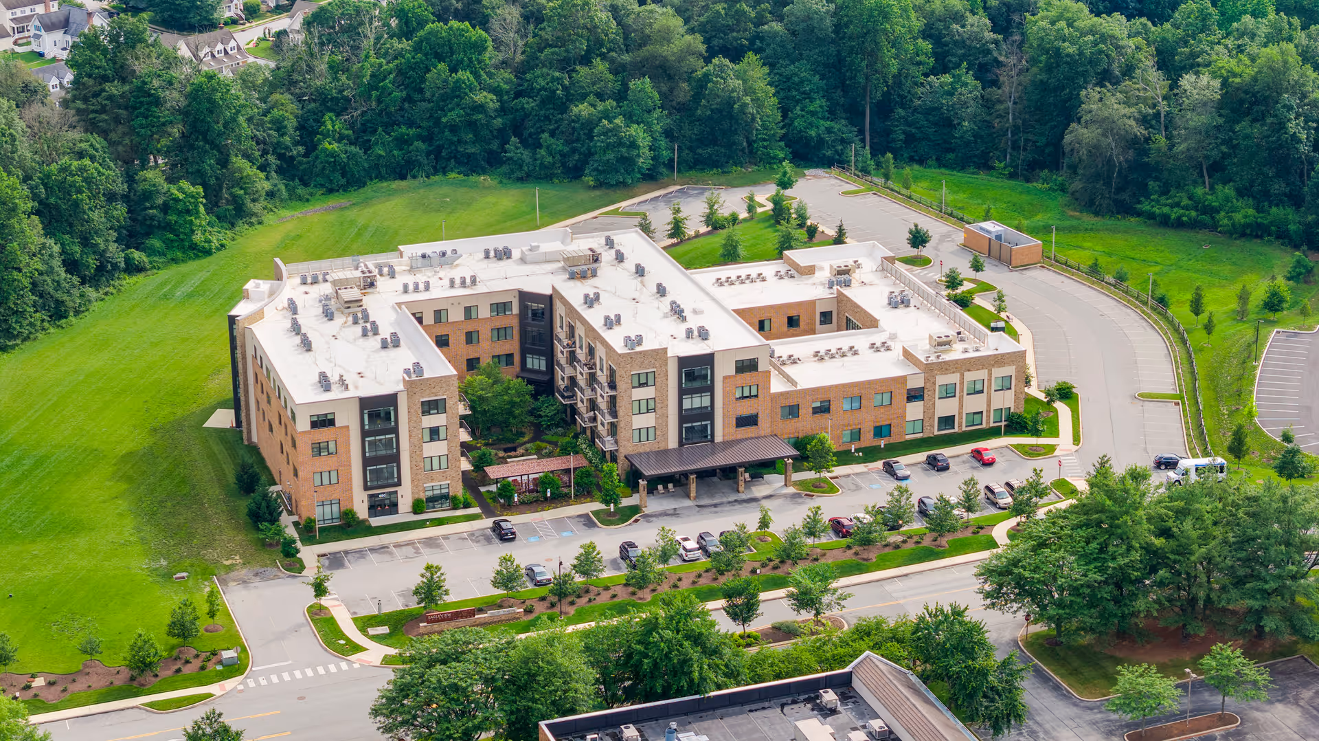 Aerial view of Eagleview Landing, a large three-story senior living facility surrounded by greenery and trees. The building has a U-shaped layout with a parking lot in front and well-maintained landscaping around it.