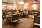 Spacious wood-paneled dining room with multiple round tables and upholstered chairs beneath chandeliers.